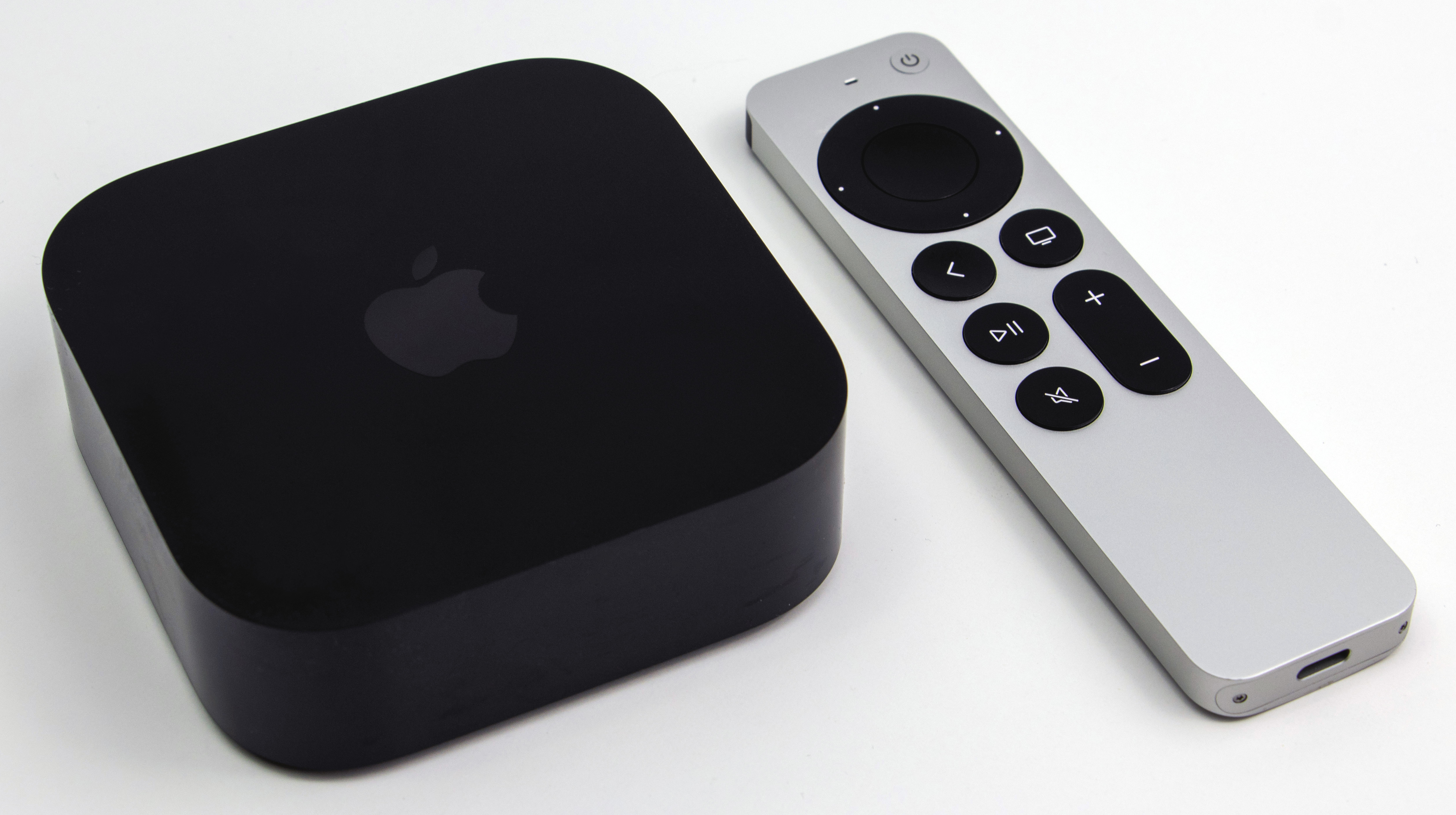 A black third-generation Apple TV 4K beside its silver Siri Remote on a white surface.