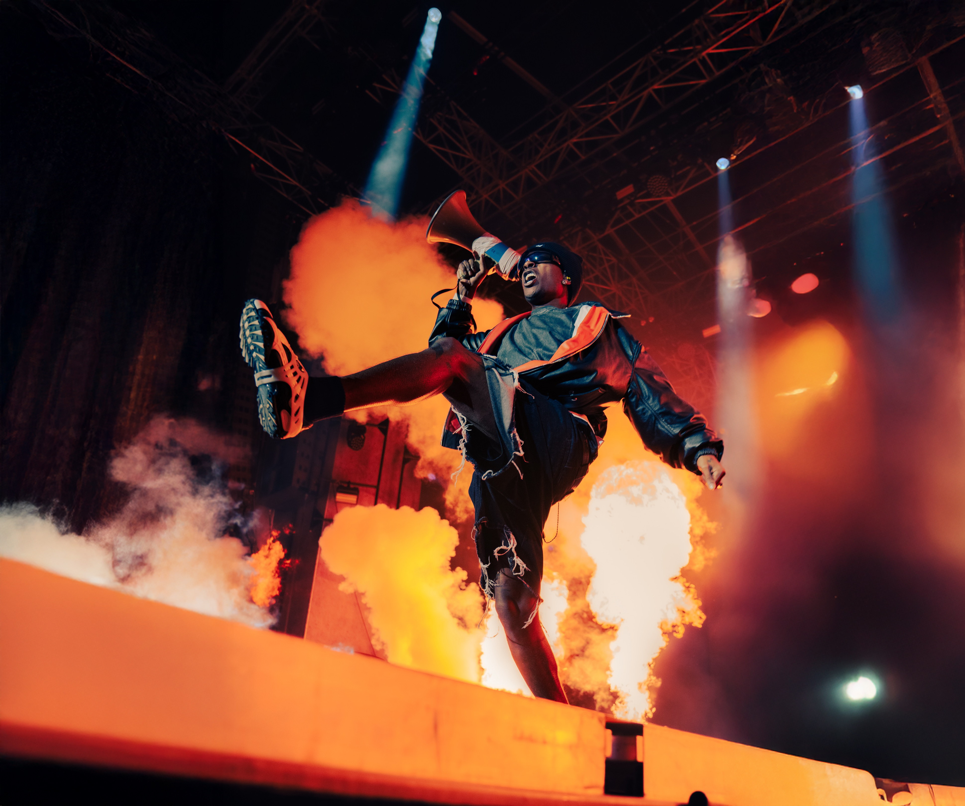 A$AP Rocky performing on stage with a megaphone, lights and orange smoke.