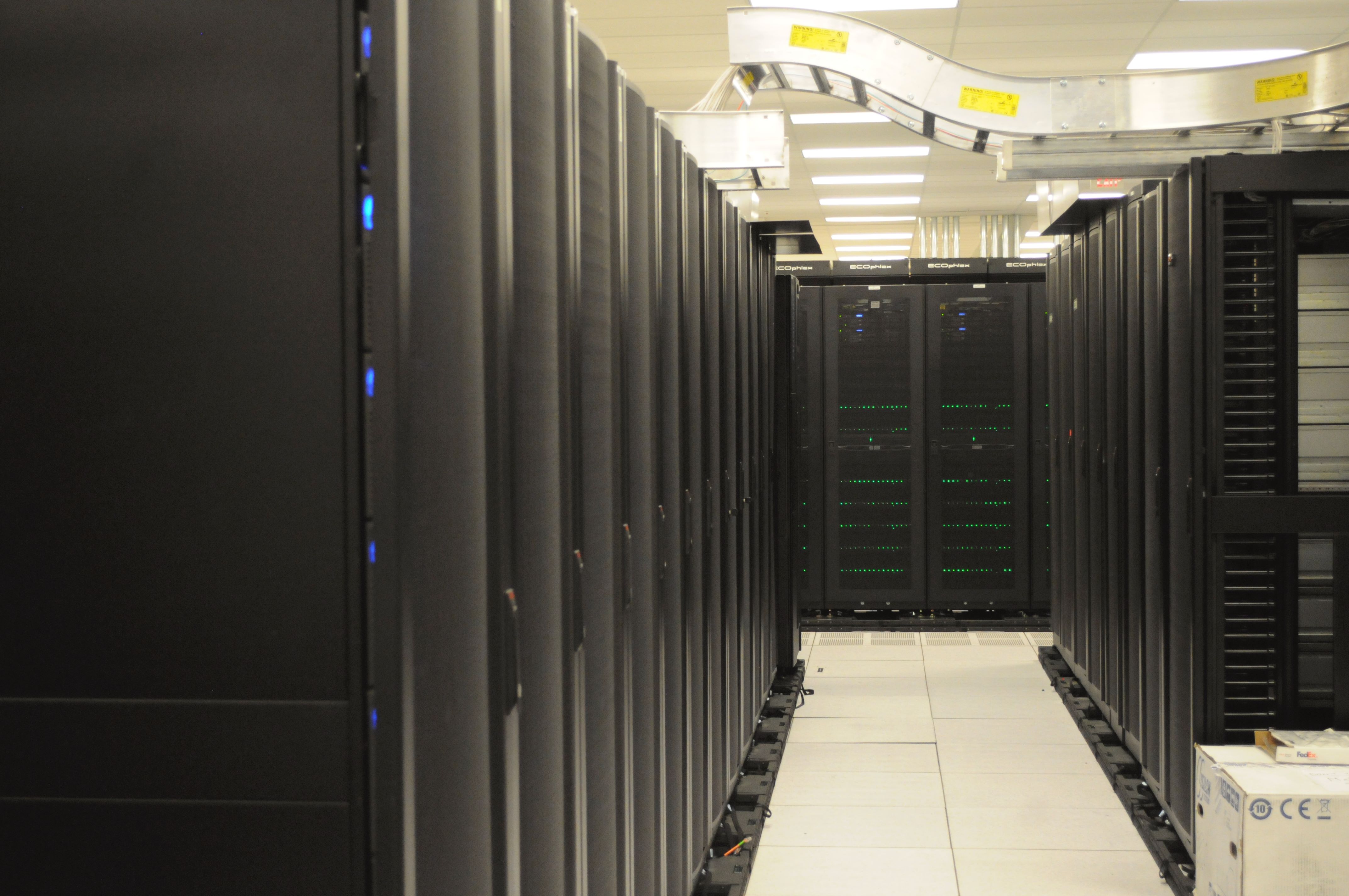 Rows of computer racks with an aisle and overhead cabling at NERSC.