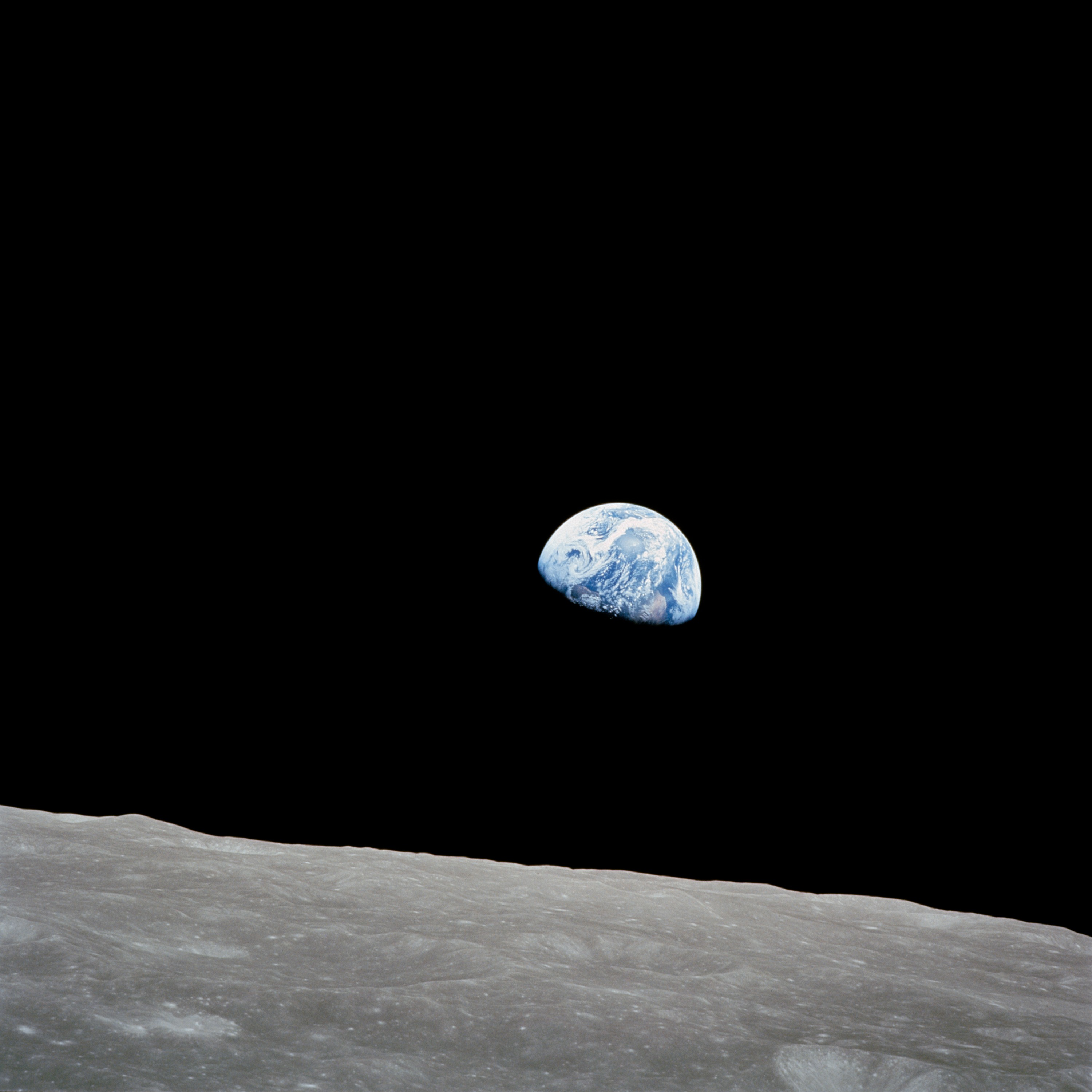 The blue-and-white Earth appears above a gray, cratered lunar horizon against black space in Bill Anders’s Apollo 8 Earthrise photograph.