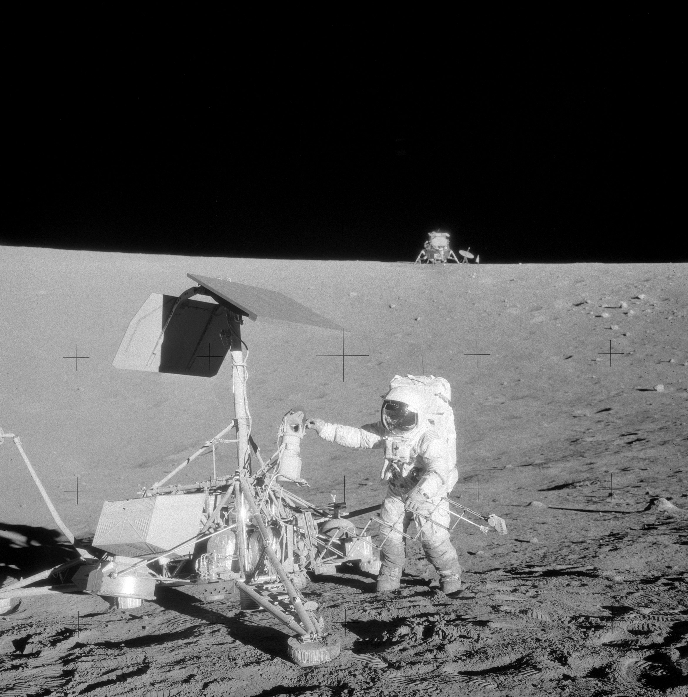 Pete Conrad stands beside the Surveyor 3 spacecraft on the Moon, with the Apollo 12 lunar module Intrepid visible on the distant crater rim.