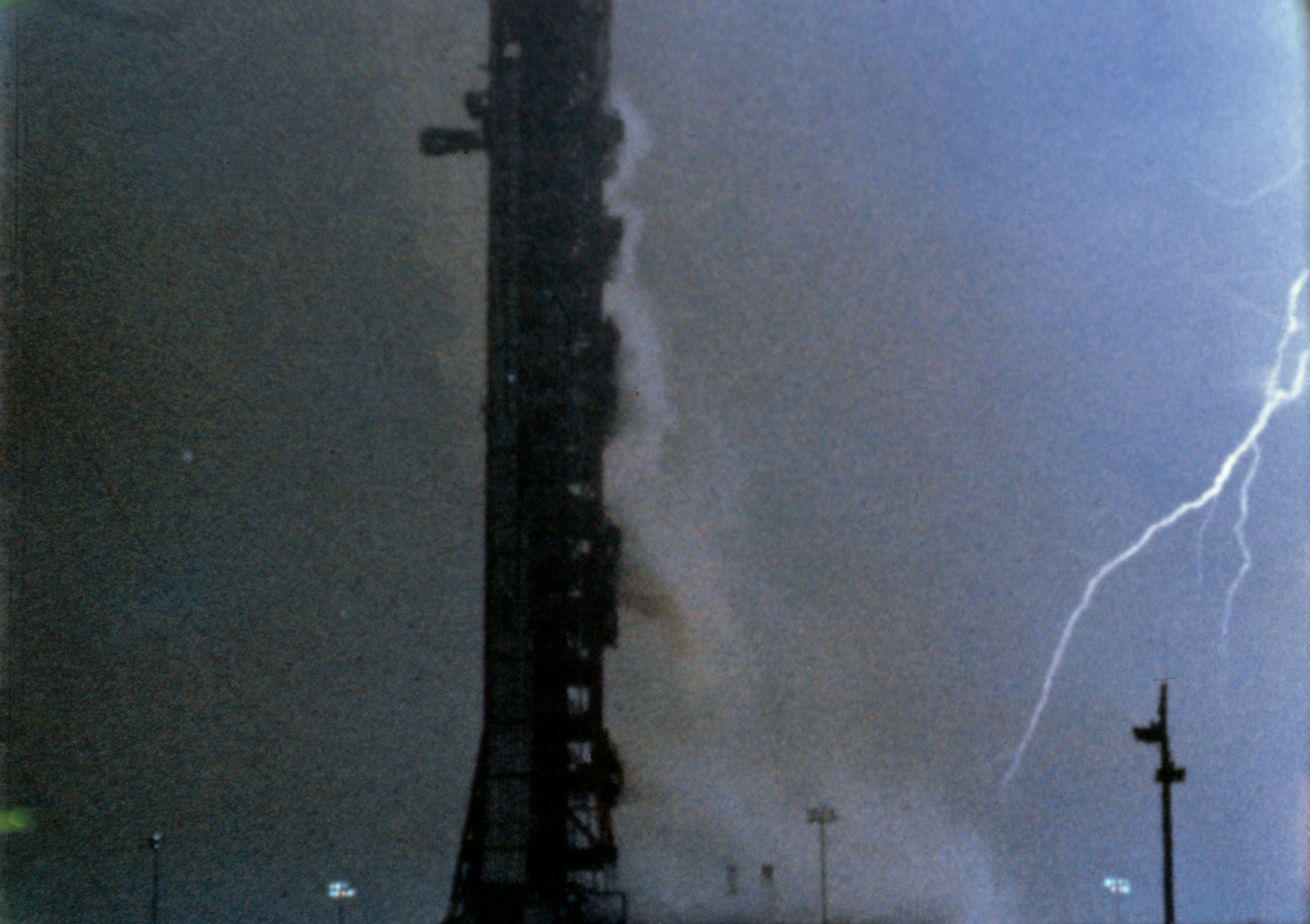A lightning bolt cuts through rainy skies beside the Apollo 12 launch tower shortly after liftoff at Launch Pad 39A.