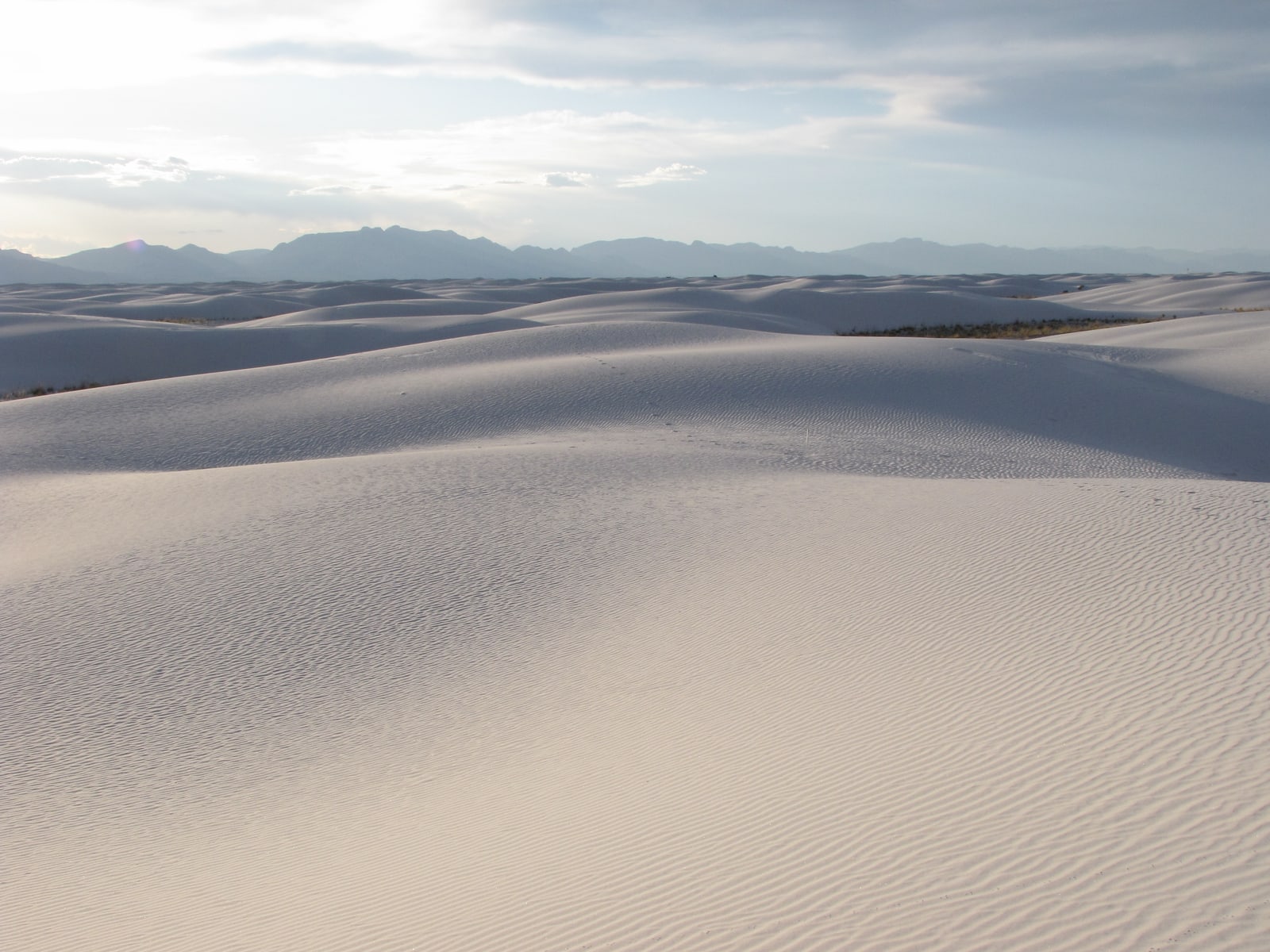 The vast, undulating sand dunes go as far as the eye can see. The San Andres mountains rise over the dunes in the background.