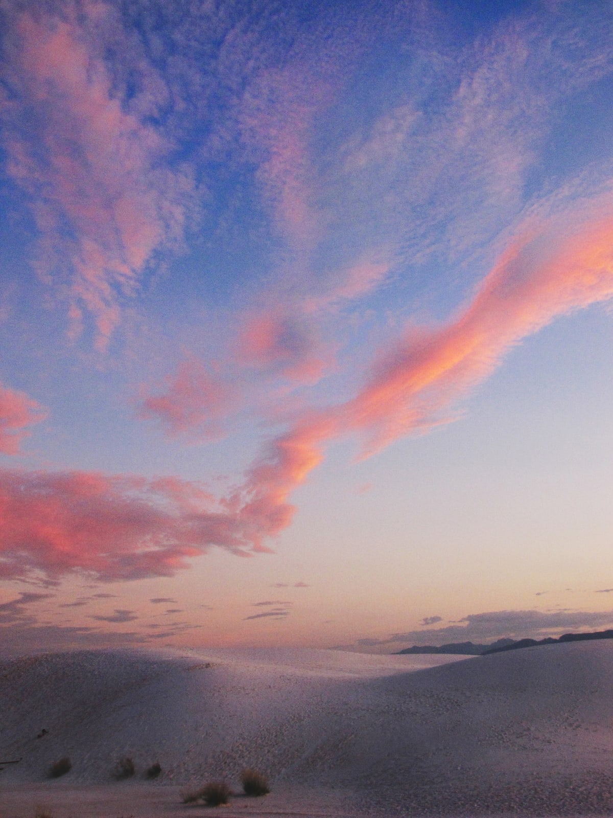 Lines of coral, pink, and orange clouds in a deep blue sky over the dune field.